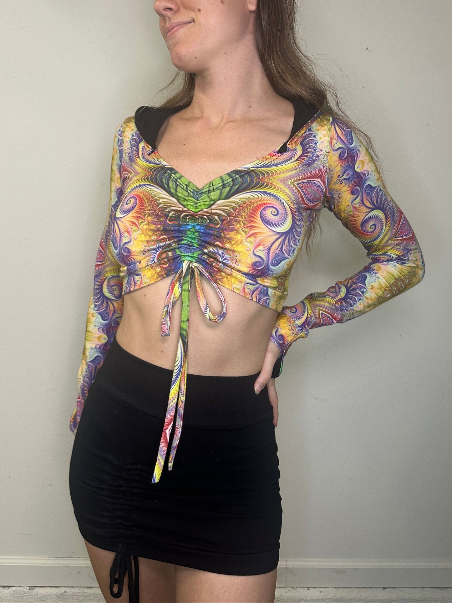 Woman wearing a colorful tie-dye long-sleeve top and black shorts on a plain background