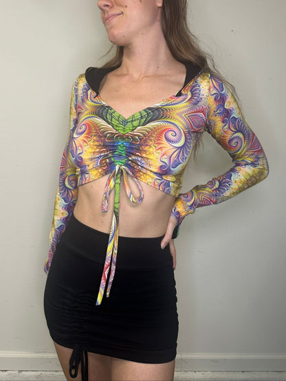 Woman wearing a colorful tie-dye long-sleeve top and black shorts on a plain background